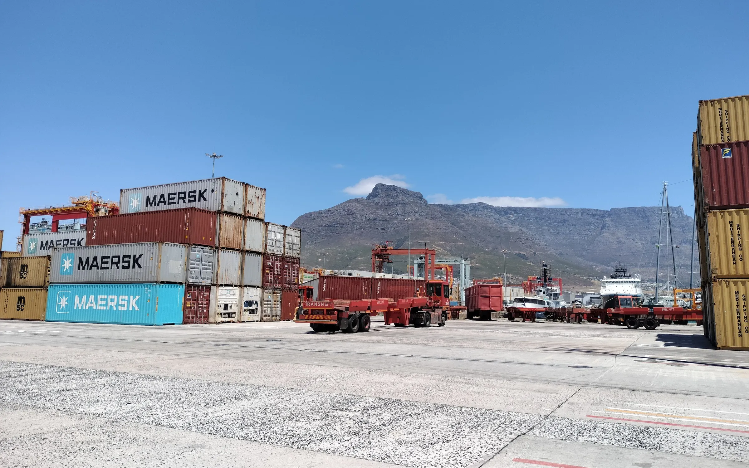 Devil's Peak and Table Mountain framed between container stacks at the Cape Town container terminal, with Transnet trailers working the apron